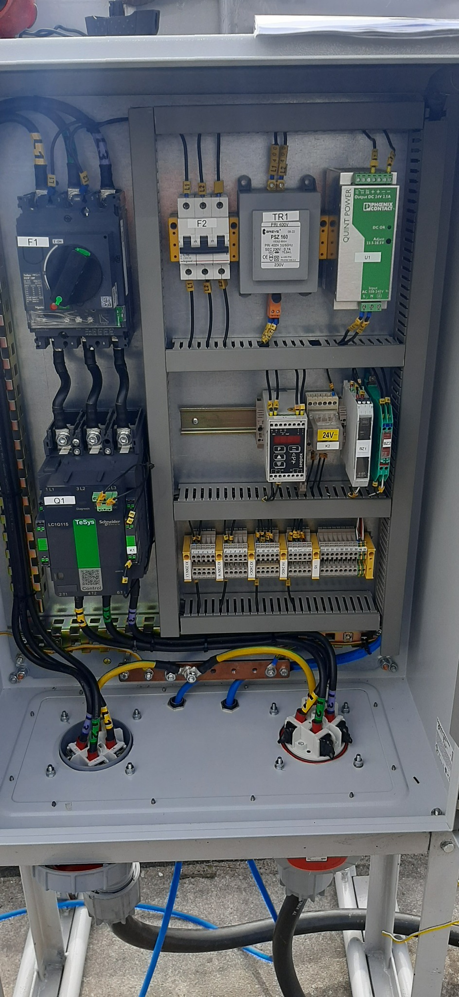 Rozdzielnica elektryczna z zainstalowanymi elementami, widoczne bezpieczniki, transformator, zasilacz oraz sterownik TeSys Schneider, okablowanie z oznaczeniami faz.