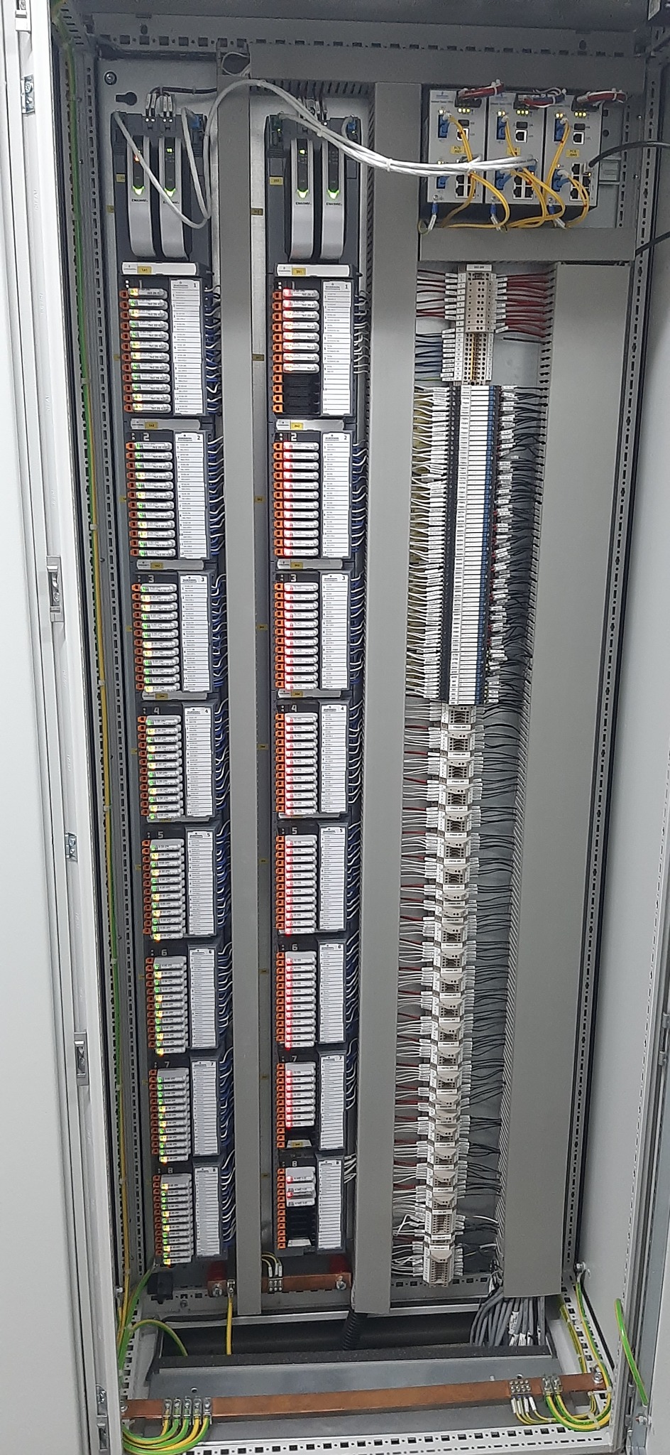 Wnętrze szafy sterowniczej z modułami PLC, okablowaniem i listwami zaciskowymi, widoczne diody sygnalizacyjne i uziemienie.