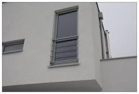 Zewnętrzna barierka ochronna z poziomych prętów zamontowana przy oknie na elewacji budynku. Widoczne są również fragmenty balkonu z metalową konstrukcją.