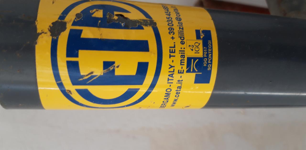 Szary element konstrukcyjny z żółtą etykietą firmy CETA, zawierającą logo, dane kontaktowe i oznaczenia jakościowe, widoczne ślady użytkowania.