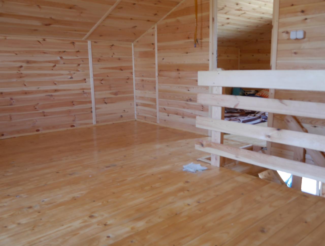 Surowe wnętrze domu szkieletowego z widoczną antresolą i drewnianymi ścianami oraz podłogą, w trakcie wykańczania.