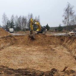 Perfect Home - Żółta koparka w trakcie prac ziemnych związanych z wykopem pod fundamenty, widoczne deski szalunkowe i biały samochód dostawczy w tle.