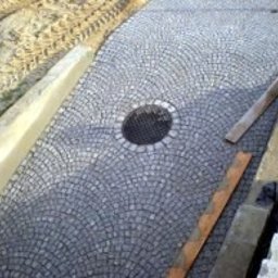 Perfect Home - Ułożona z szarej kostki granitowej aleja w kształcie wachlarza z okrągłą studzienką kanalizacyjną pośrodku, widoczne deski i świeżo wylany beton.