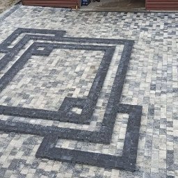 Perfect Home - Ułożona kostka brukowa z dekoracyjnym wzorem geometrycznym z ciemnych kostek, widok z góry, teren wokół częściowo zagospodarowany, w tle widoczny garaż.