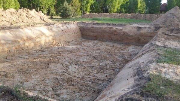 Wykonany wykop pod fundamenty domu jednorodzinnego, widoczne warstwy ziemi i pryzmy ziemi usypane wokół wykopu.