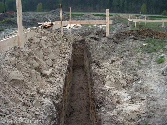 Wykop pod fundamenty domu jednorodzinnego z drewnianym szalunkiem w tle, widok z góry.