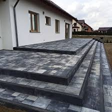 Ułożona kostka brukowa na tarasie i schodach przed domem w Czerwionce-Leszczynach. Widoczne szare i czarne kostki tworzące wzór na powierzchni.