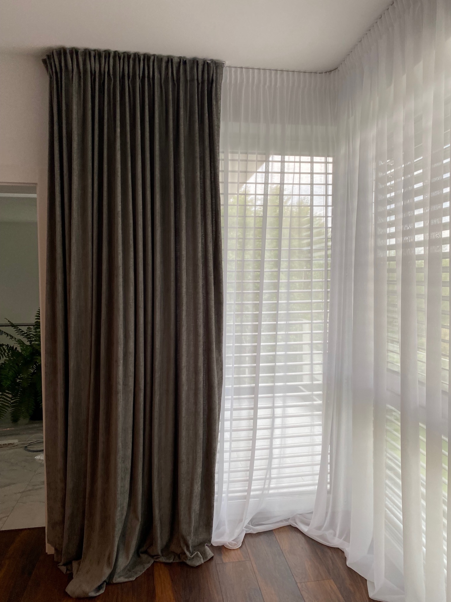 Eleganckie, długie zasłony: grafitowa, aksamitna po lewej i zwiewna, biała, woalowa po prawej, w rogu pokoju z drewnianą podłogą. Subtelne światło.