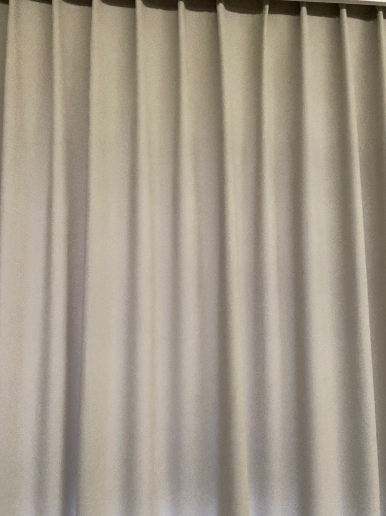 Delikatna, beżowa zasłona z subtelnymi fałdami, zawieszona na karniszu. Stonowana kolorystyka, miękkie światło podkreśla strukturę tkaniny. Minimalistyczny i elegancki element wystroju.