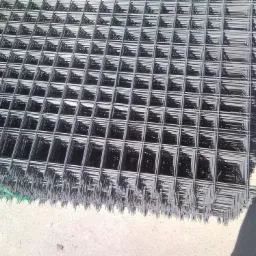 Stos zgrzewanych mat z drutu, zabezpieczonych zieloną taśmą, na betonowej powierzchni w jasnym świetle słonecznym.