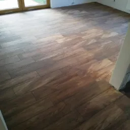 Ułożona podłoga z paneli imitujących drewno w nowym, jasnym pokoju z dużym oknem balkonowym i białymi ścianami.