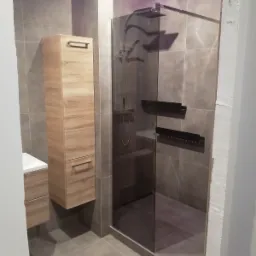 Nowoczesna łazienka z kabiną prysznicową typu walk-in, szafką z umywalką w odcieniach drewna i podświetleniem LED w suficie, płytki w odcieniach szarości.