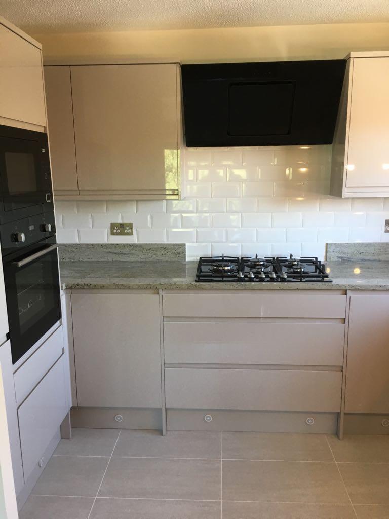 Jasna kuchnia z białymi płytkami metra i czarnym okapem, widok na płytę gazową i zabudowę szafek z szufladami.