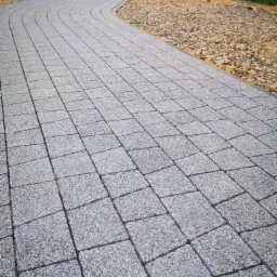 Ścieżka z szarej kostki granitowej ułożona w łuk, obok wysypany żwir, widok z g&oacute;ry.