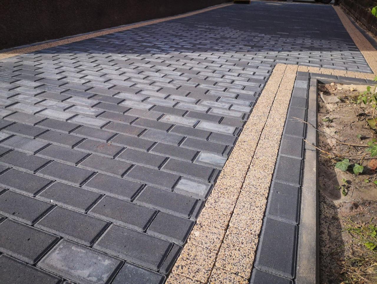 Ułożona szara kostka brukowa w jodełkę, obrzeża z jasnego kruszywa, widok na podjazd.