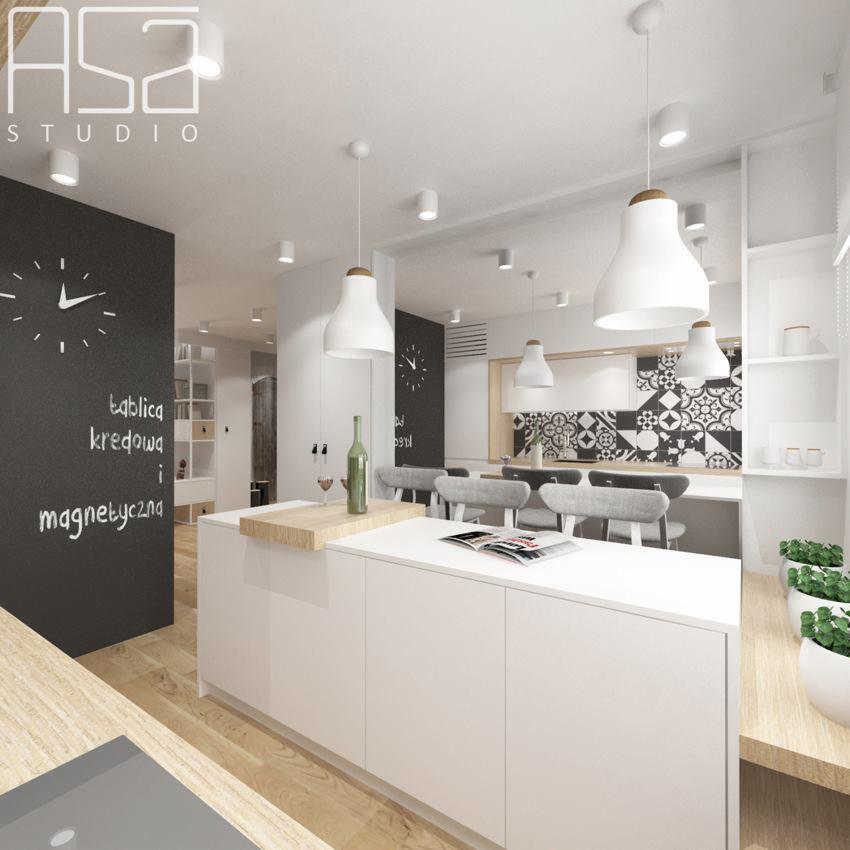 Wnętrze nowoczesnej kuchni z białą wyspą, wiszącymi lampami z drewnianymi akcentami, tablicą kredową z zegarem i napisem, oraz wzorzystą ścianą w tle.