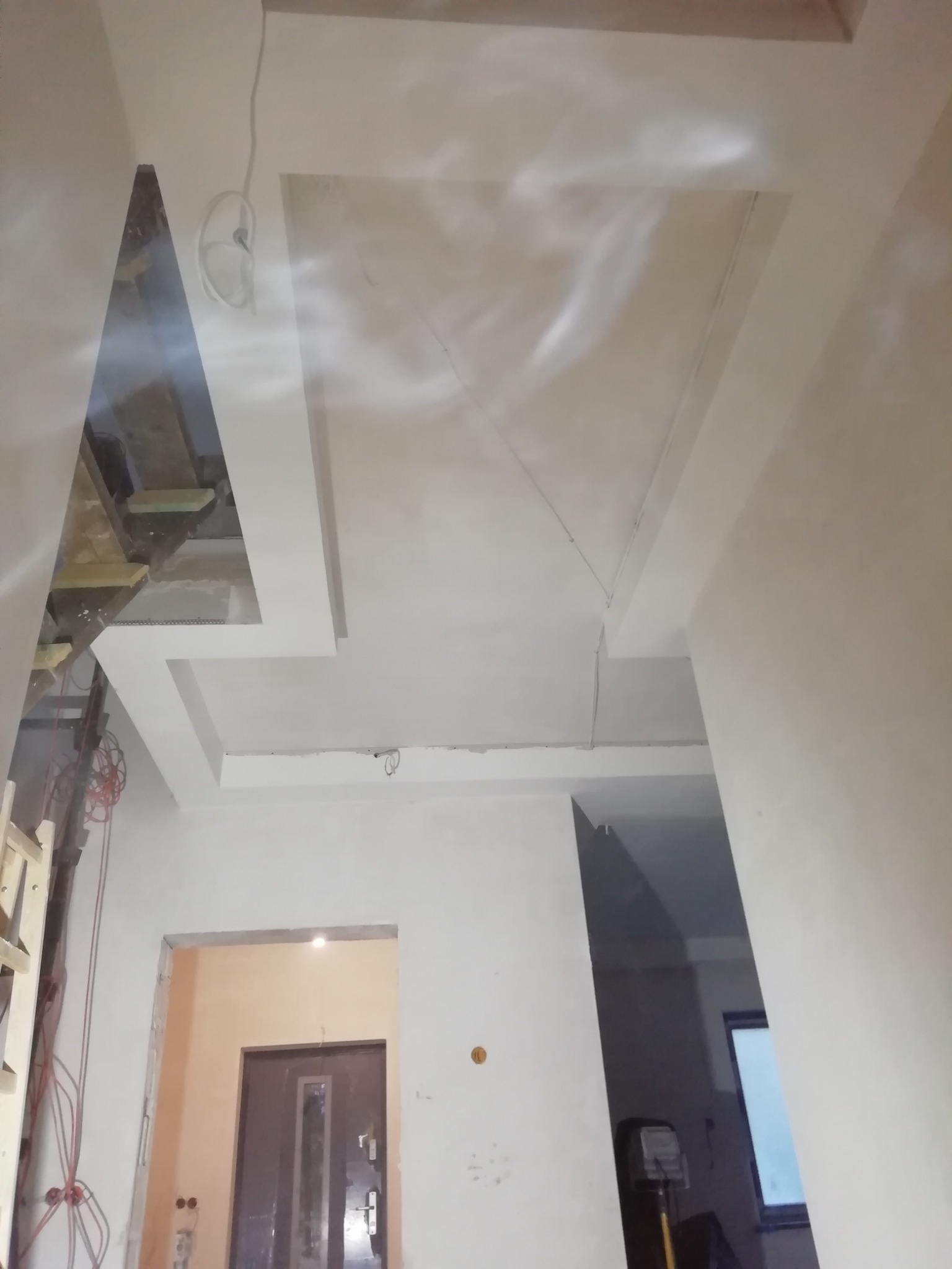 Skomplikowana konstrukcja sufitu podwieszanego z widocznymi elementami instalacji elektrycznej i fragmentem pomieszczenia z drzwiami w tle.