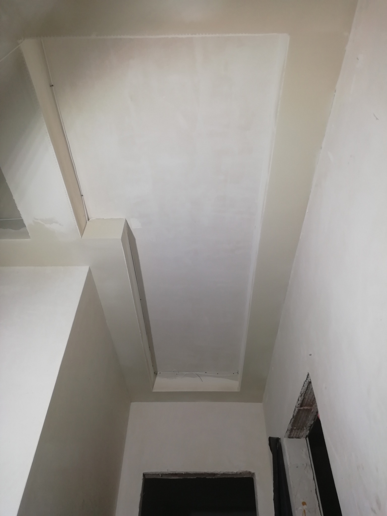 Świeżo wykończony sufit podwieszany z płyt kartonowo-gipsowych, widok z dołu, widoczne kable w suficie i fragment otworu drzwiowego w ścianie.