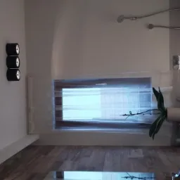 Nowoczesna łazienka z drewnopodobną podłogą, oświetleniem punktowym na ścianie, oknem z delikatną firanką i rośliną w doniczce, widok na kabinę prysznicową.