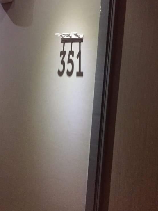 Numer 351 na drzwiach z metalowymi cyframi, oświetlony od góry, widok z bliska.