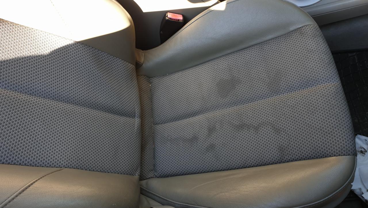 Szare, tekstylne siedzenie samochodowe z widocznymi plamami i zabrudzeniami, oświetlone z góry.