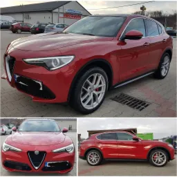 Czerwony samochód Alfa Romeo Stelvio, widok z przodu i z boku, zaparkowany na kostce brukowej przed budynkiem z apteką i drogerią.