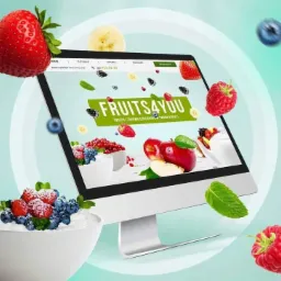 Monitor wyświetlający stronę internetową z motywem owocowym, otoczony truskawkami, malinami, borówkami i miseczką z deserem owocowym.