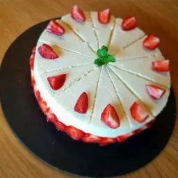 Tort śmietankowy z truskawkami, podzielony na r&oacute;wne porcje, udekorowany miętą na czarnym talerzu.