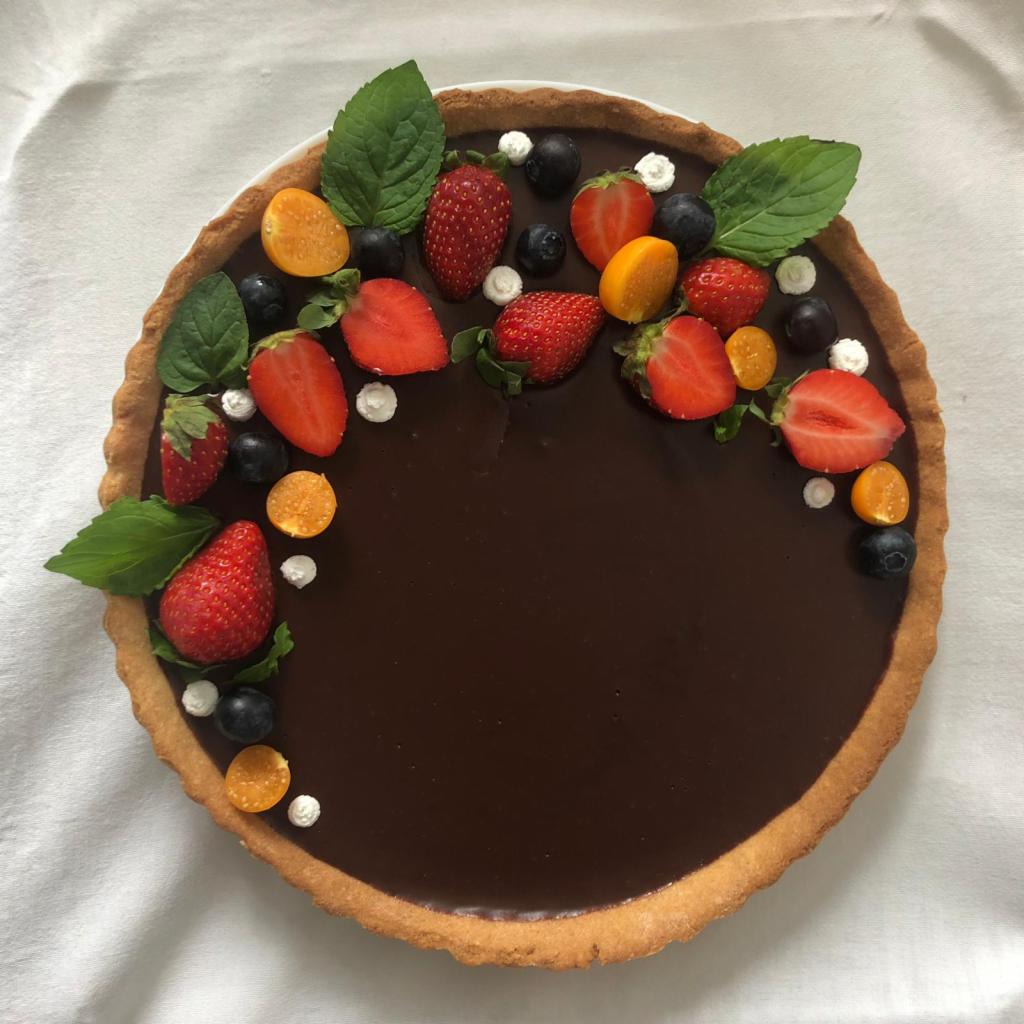 Tarta z kremem czekoladowym, udekorowana świeżymi truskawkami, borówkami, miechunką peruwiańską i listkami mięty, z delikatnymi kleksami bitej śmietany.