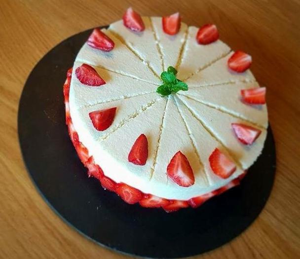 Tort śmietankowy z truskawkami, podzielony na równe porcje, udekorowany miętą na czarnym talerzu.