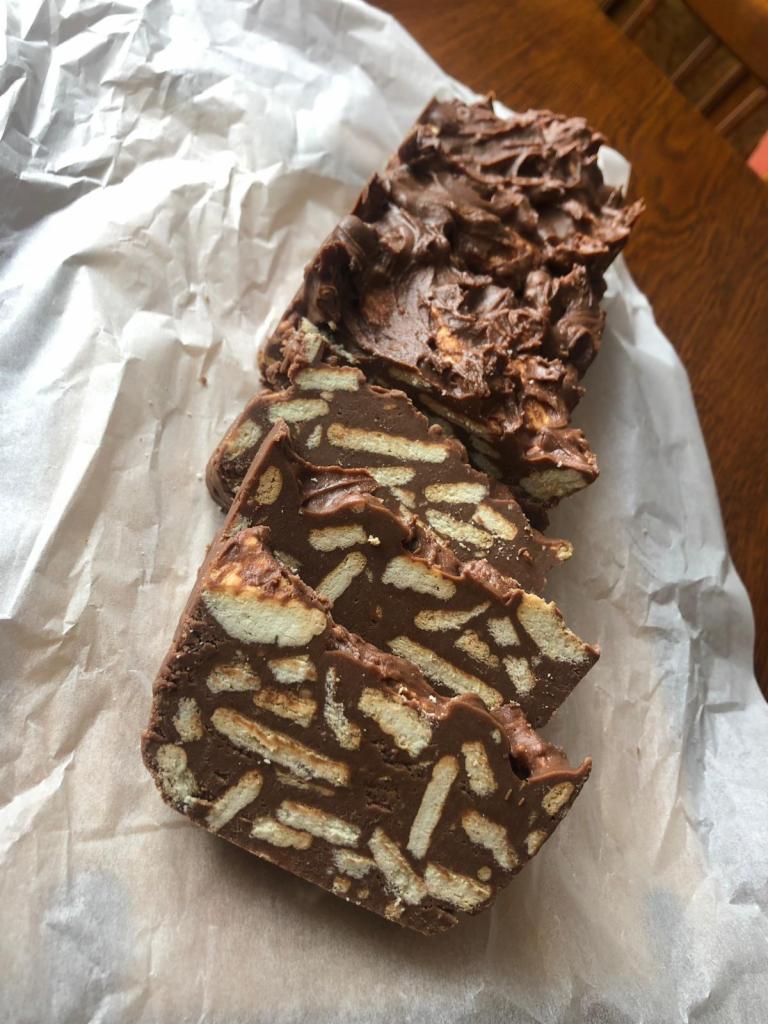 Domowe ciasto czekoladowe z herbatnikami na papierze pergaminowym, widoczne nieregularne kawałki i gruba warstwa polewy.