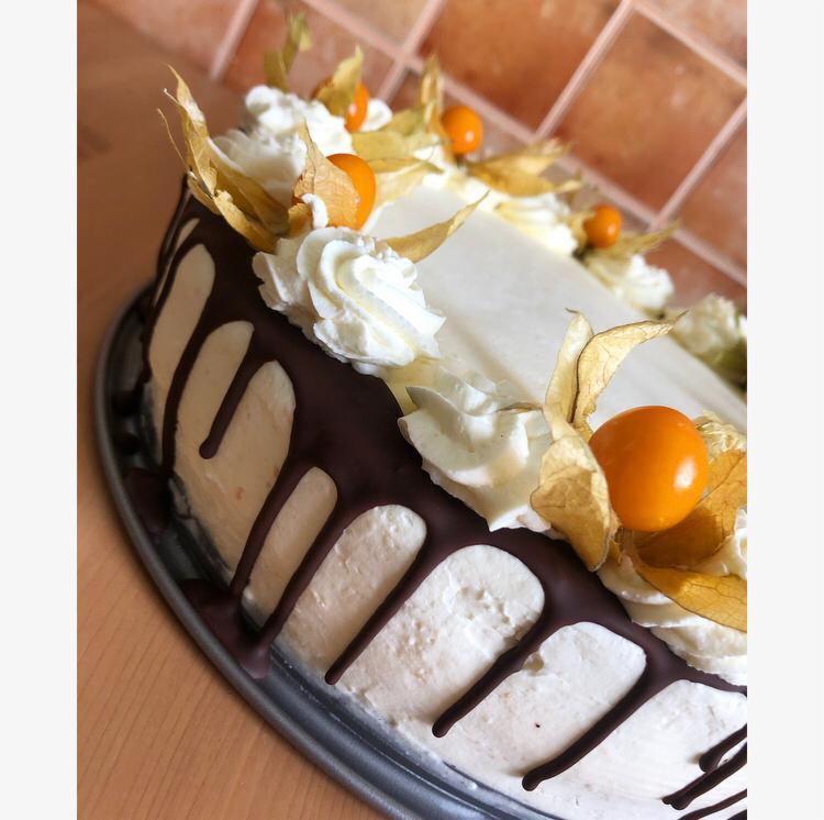 Tort z kremem, polewą czekoladową i dekoracją z miechunki peruwiańskiej, ustawiony na metalowej tacy.