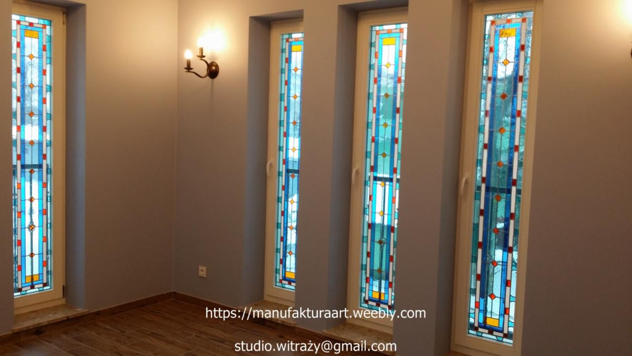 Wnętrze z czterema wysokimi oknami z witrażami w stylu art deco, oświetlonymi przez kinkiet na ścianie.