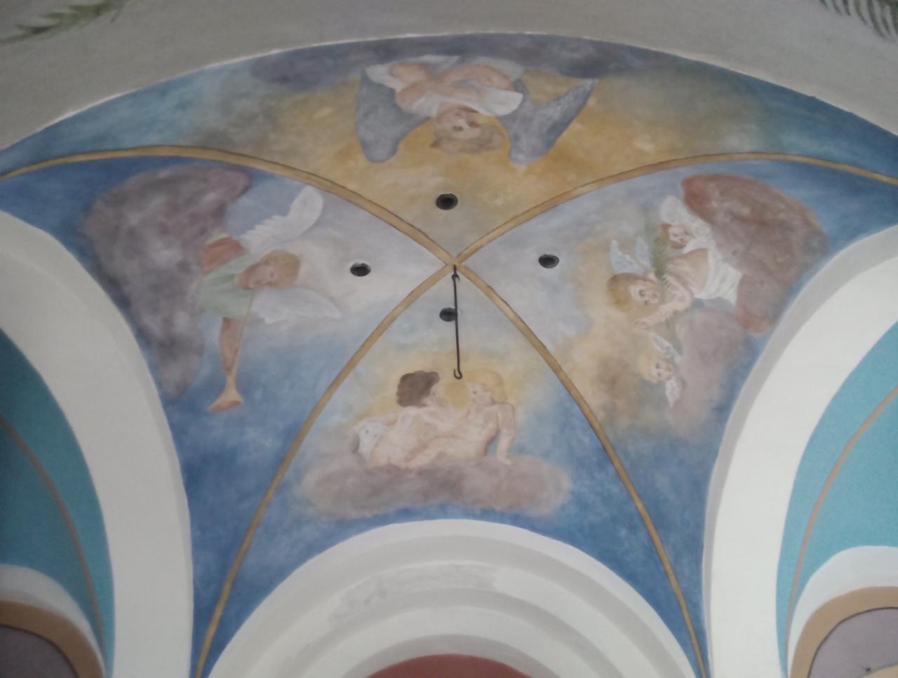 Malowidło sufitowe w kościele przedstawiające anioły w różnych pozach, wykonane w jasnych, pastelowych kolorach na tle błękitnego nieba, z widocznymi elementami architektury łukowej i oświetleniem...