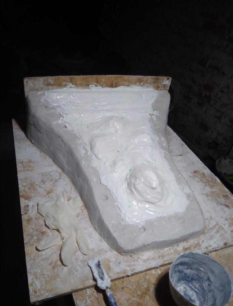 Forma odlewnicza wypełniona gipsem, widoczne narzędzia i rękawice ochronne, przygotowana do wykonania repliki elementu architektonicznego.