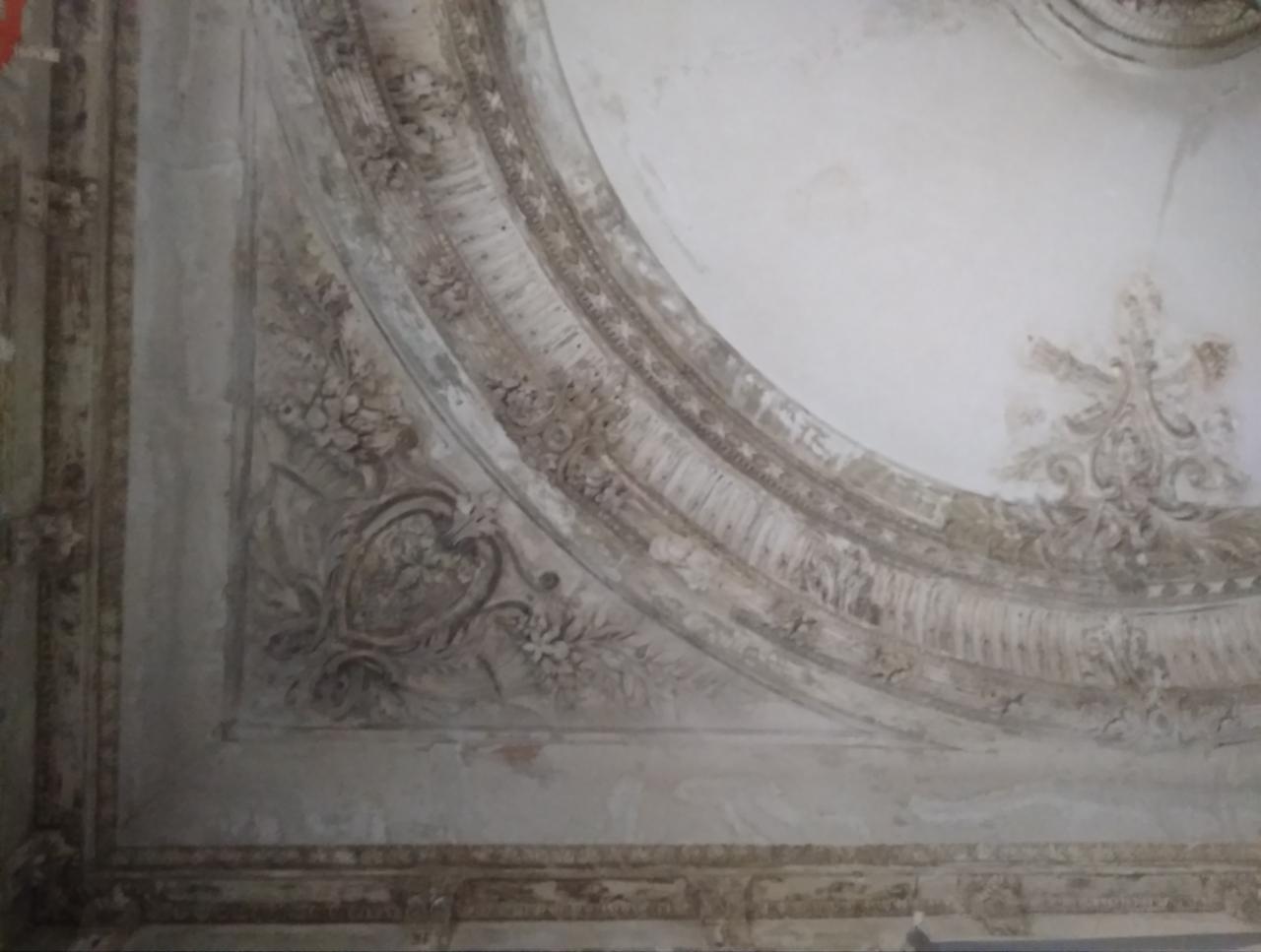 Fragment zdobionego sufitu z ornamentami w stylu klasycystycznym, widoczne ślady upływu czasu i braków w tynku.