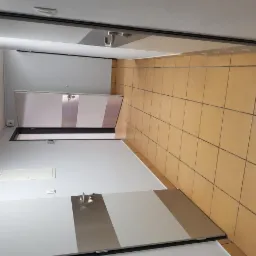 Korytarz z beżową terakotą, białymi ścianami i dwoma drzwiami z metalowymi panelami, widok z góry.