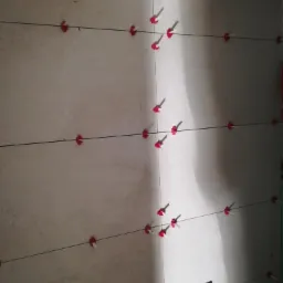 Świeżo ułożone, beżowe płytki ścienne z czerwonymi klipsami poziomującymi i czarnymi sznurkami, widoczny poziomica w rogu.