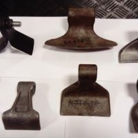 Zestaw metalowych zębów roboczych do maszyn budowlanych, widoczne ślady użytkowania, różny kształt i rozmiar, ułożone na białym tle.