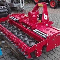 Czerwona glebogryzarka separacyjna na palecie, widoczne elementy robocze i przekładnia, w tle fragmenty ciągników.