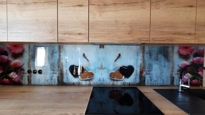 Szklany panel kuchenny z motywem wiśni na tle imitującym stare deski, wkomponowany między drewniane szafki a blat, z widocznymi gniazdkami elektrycznymi i czarną płytą indukcyjną.