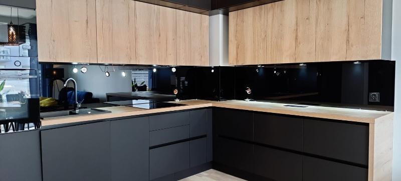 Nowoczesna kuchnia z szarymi szafkami dolnymi i drewnopodobnymi górnymi, czarny panel szklany między szafkami, oświetlenie punktowe pod szafkami.