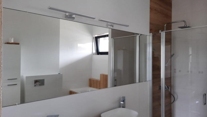 Duże lustro w łazience z oświetleniem LED nad umywalką, odbijające wnętrze z wanną i kabiną prysznicową.