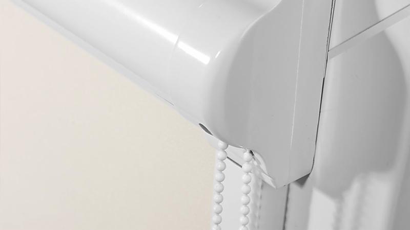 Szczegółowe ujęcie mechanizmu zwijania białej rolety z łańcuszkiem kulkowym na tle jasnej ściany.