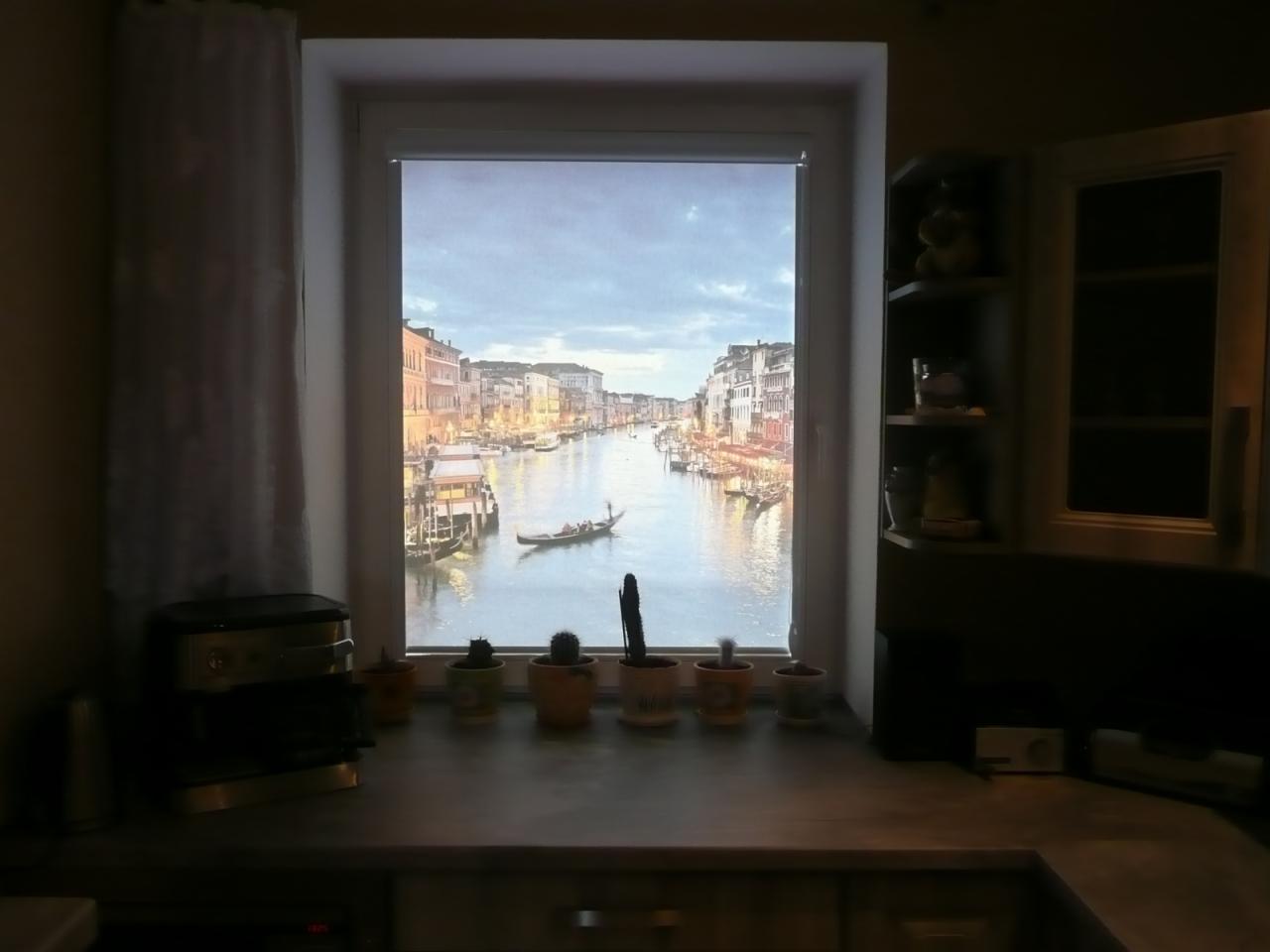 Kuchnia z widokiem na wenecki kanał przez okno z zamontowaną przesłoną z nadrukiem, na parapecie doniczki z sukulentami i ekspres do kawy.