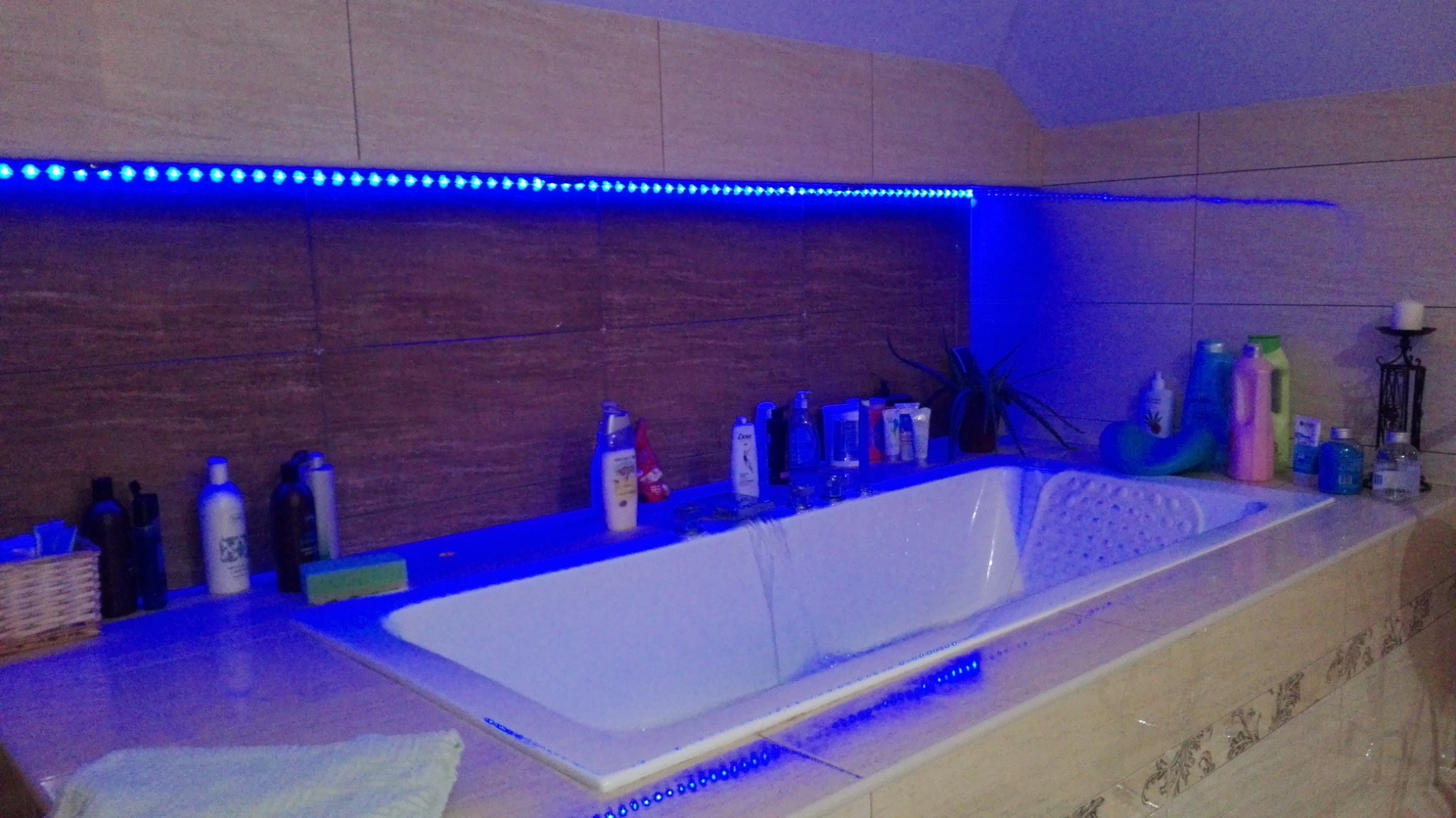 Wanna z hydromasażem, oświetlona niebieskimi diodami LED, w tle kosmetyki i płytki ceramiczne.