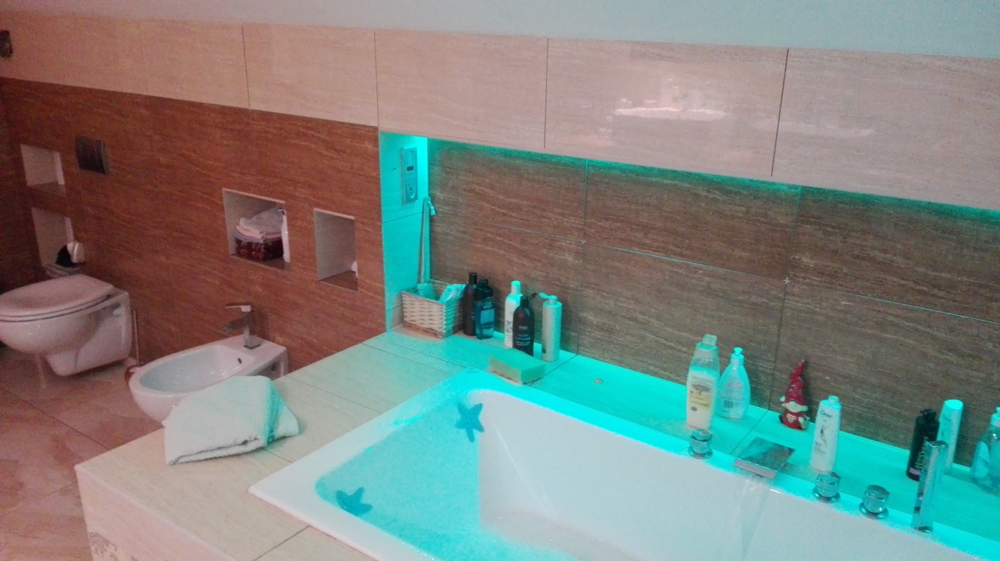 Nowoczesna łazienka z podświetleniem LED, beżowo-brązowe płytki, wanna z hydromasażem i dekoracyjnymi gwiazdkami, toaleta i bidet w tle.