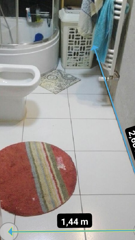 Fragment łazienki z białą armaturą, grzejnikiem drabinkowym z powieszonym ręcznikiem i okrągłym dywanikiem w ciepłych kolorach na białych płytkach podłogowych.