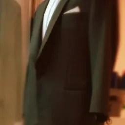 Elegancki, ciemny smoking z muchą i białą poszetką, prezentowany na manekinie w pracowni, z widocznym odbiciem drugiego smokingu w tle.