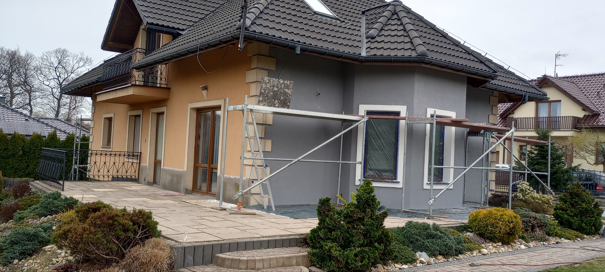 Dom w Łodygowicach częściowo otynkowany na szaro, z widocznym rusztowaniem i fragmentem elewacji w kolorze beżowym, prezentujący etap prac wykończeniowych elewacji.